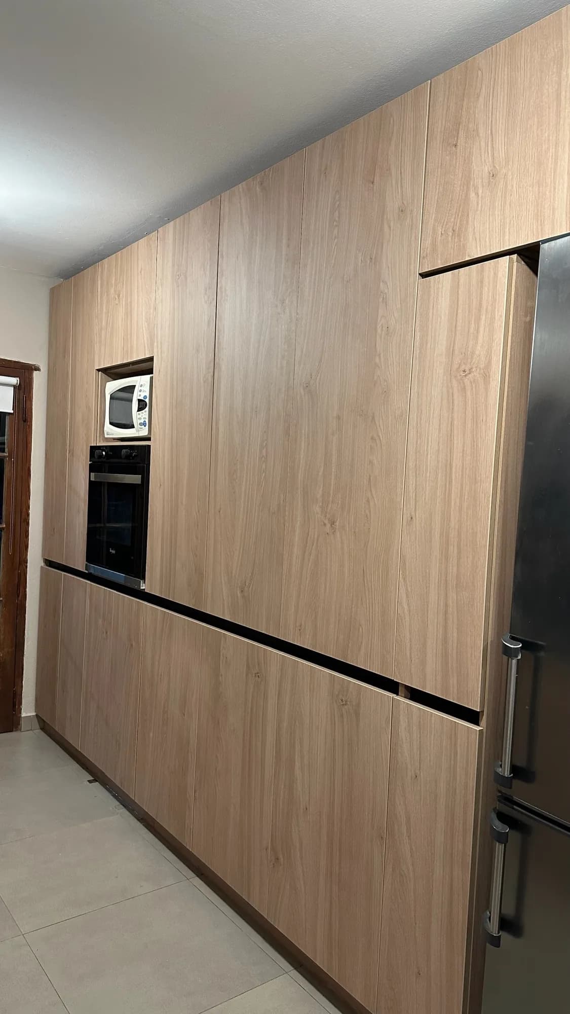 Frente de columnas y bajomesadas de melamina símil roble con horno y microondas empotrados, separadas por una línea negra; toma lateral en diagonal