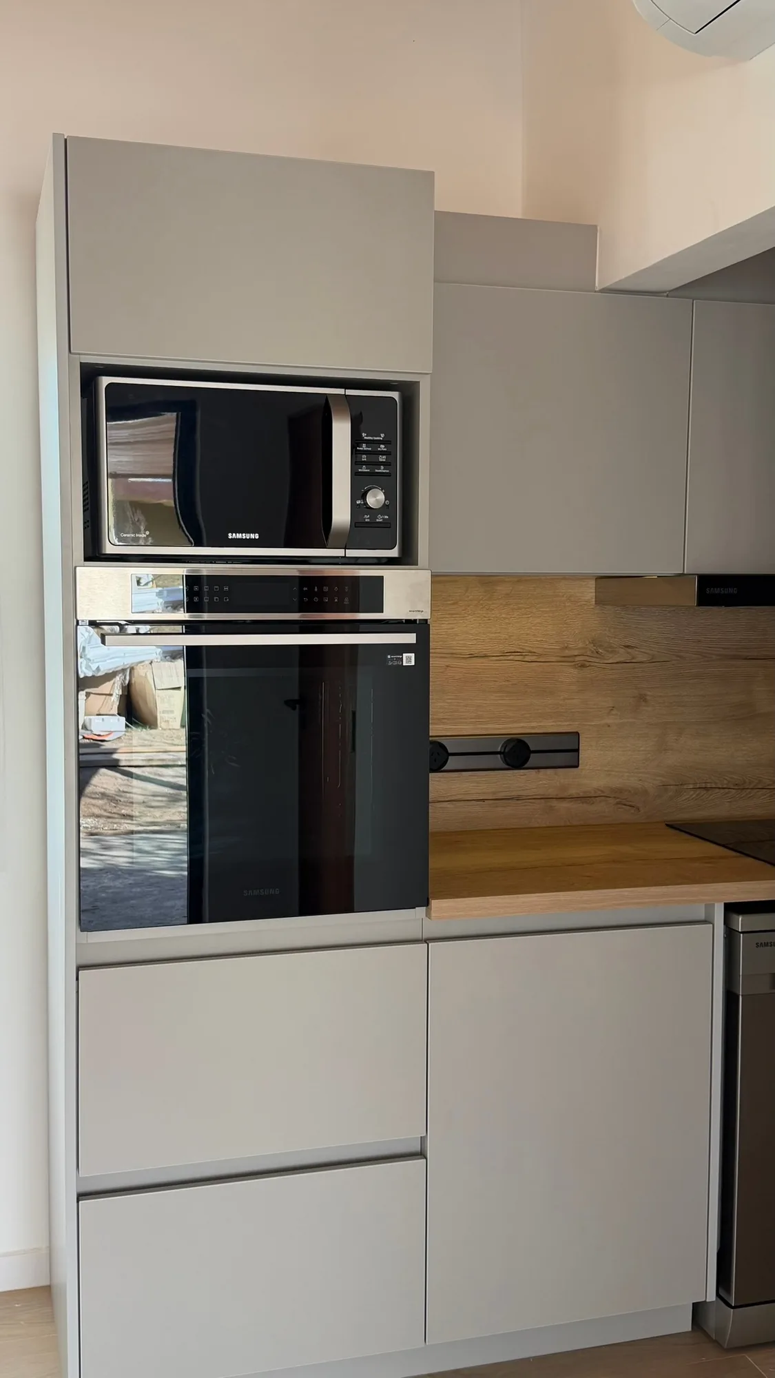 Columna de cocina con microondas y horno Samsung, alacenas, salpicadero símil madera con módulo de enchufes negro y cajones; toma frontal cercana