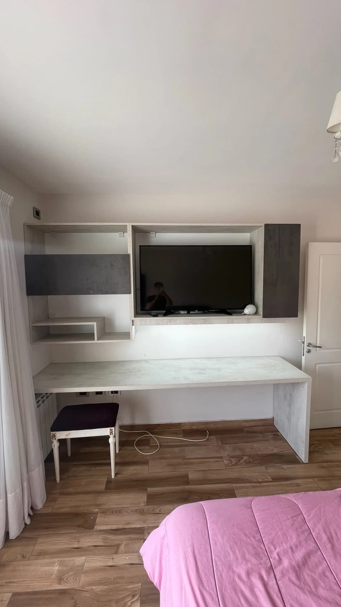 Escritorio en voladizo con estantes y módulo para TV, frentes en gris cemento y blanco, en un dormitorio con piso símil madera; toma frontal