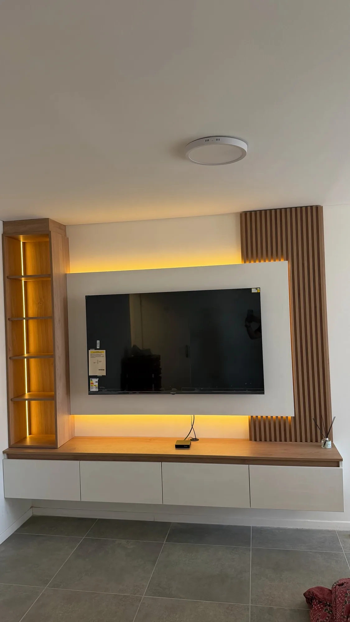 Panel de TV con marco blanco retroiluminado con LED cálido, listones de madera, biblioteca angosta con LED vertical y mesada flotante con cajones blancos; toma frontal