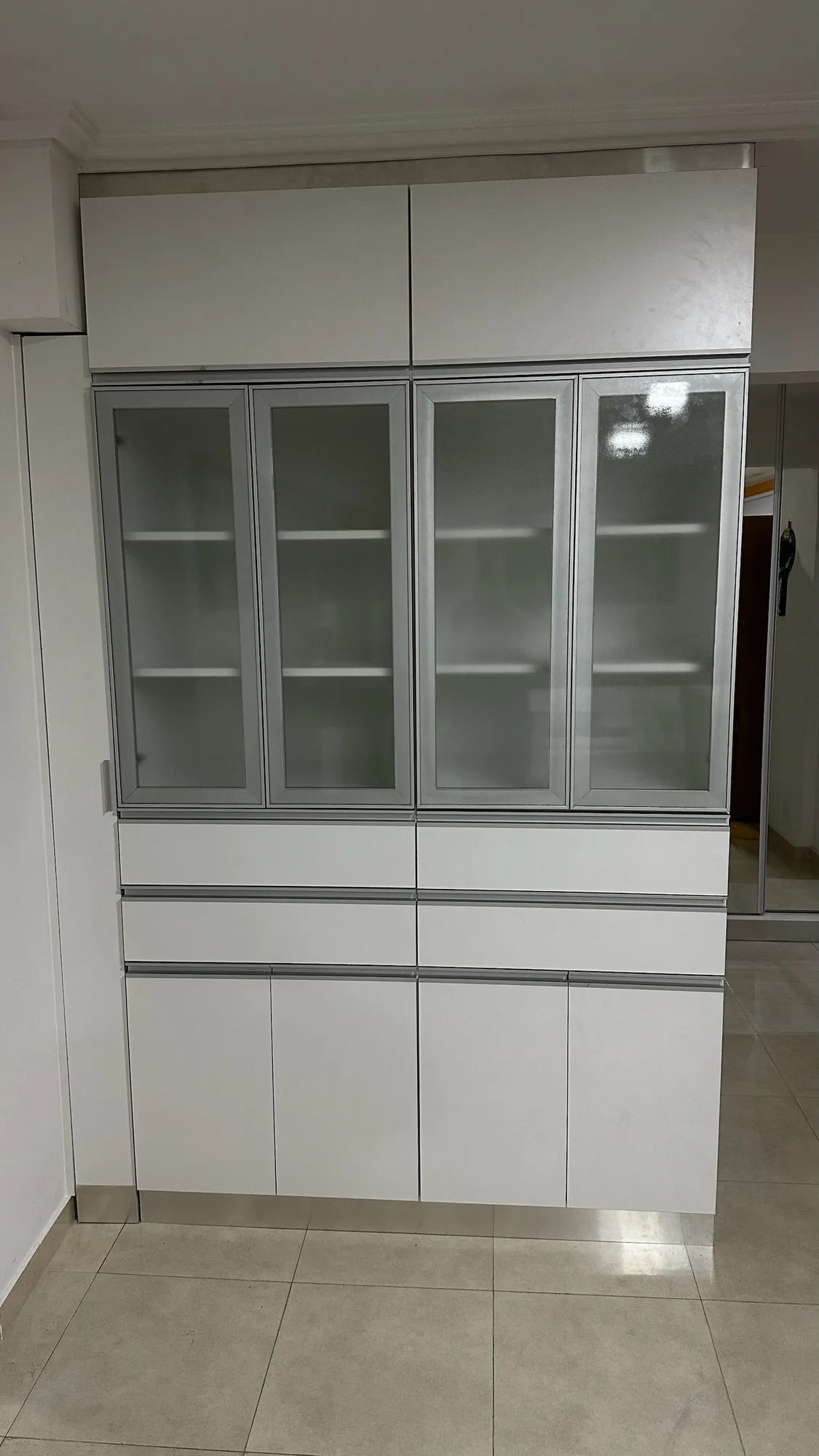 Módulo blanco hasta el techo con cuatro puertas de vidrio esmerilado con marco de aluminio, dos hileras de cajones y puertas bajas con tiradores de aluminio; toma frontal