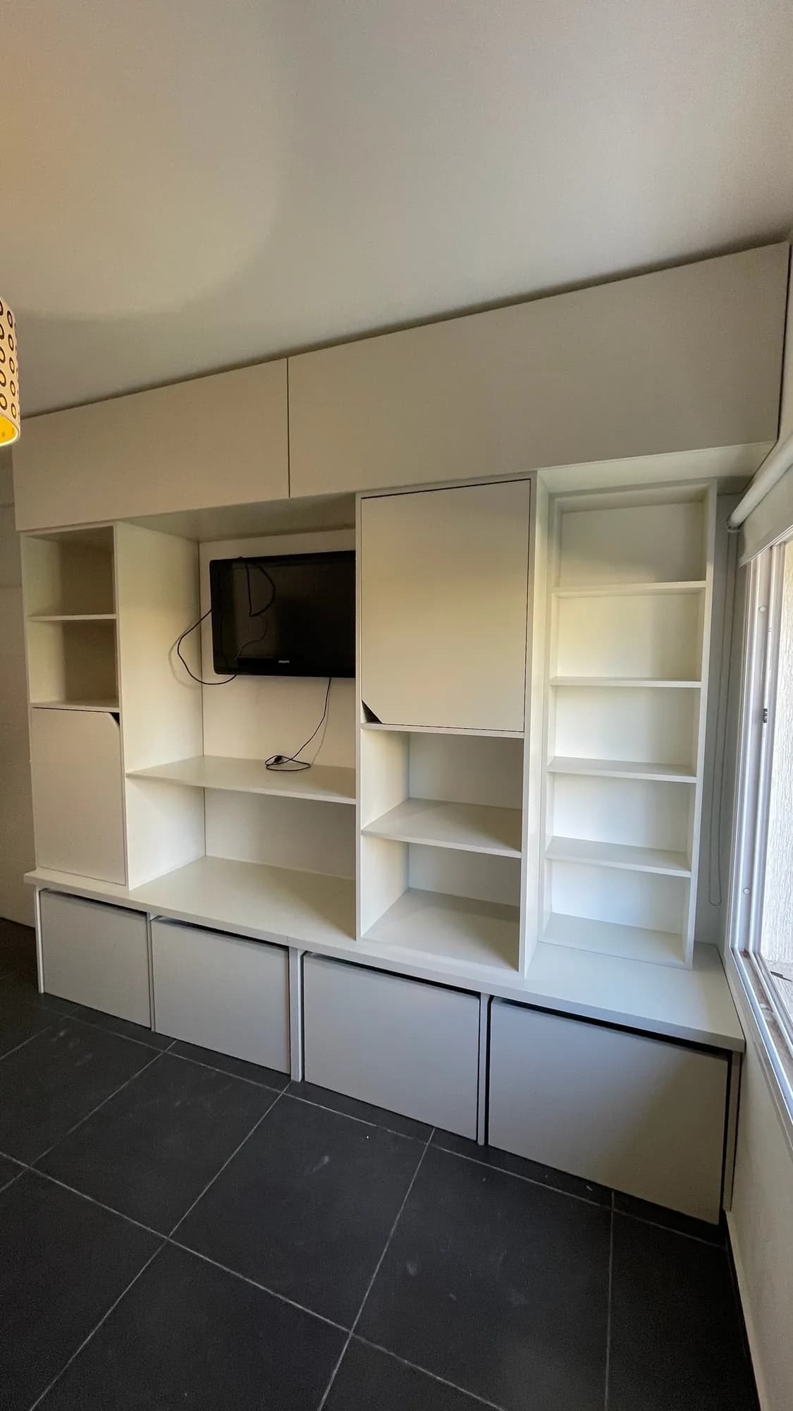 Mueble de TV de pared completa en melamina blanca y gris claro, con alacenas altas, estantes, columna de repisas y cajones bajos, con TV colgado; toma frontal en diagonal