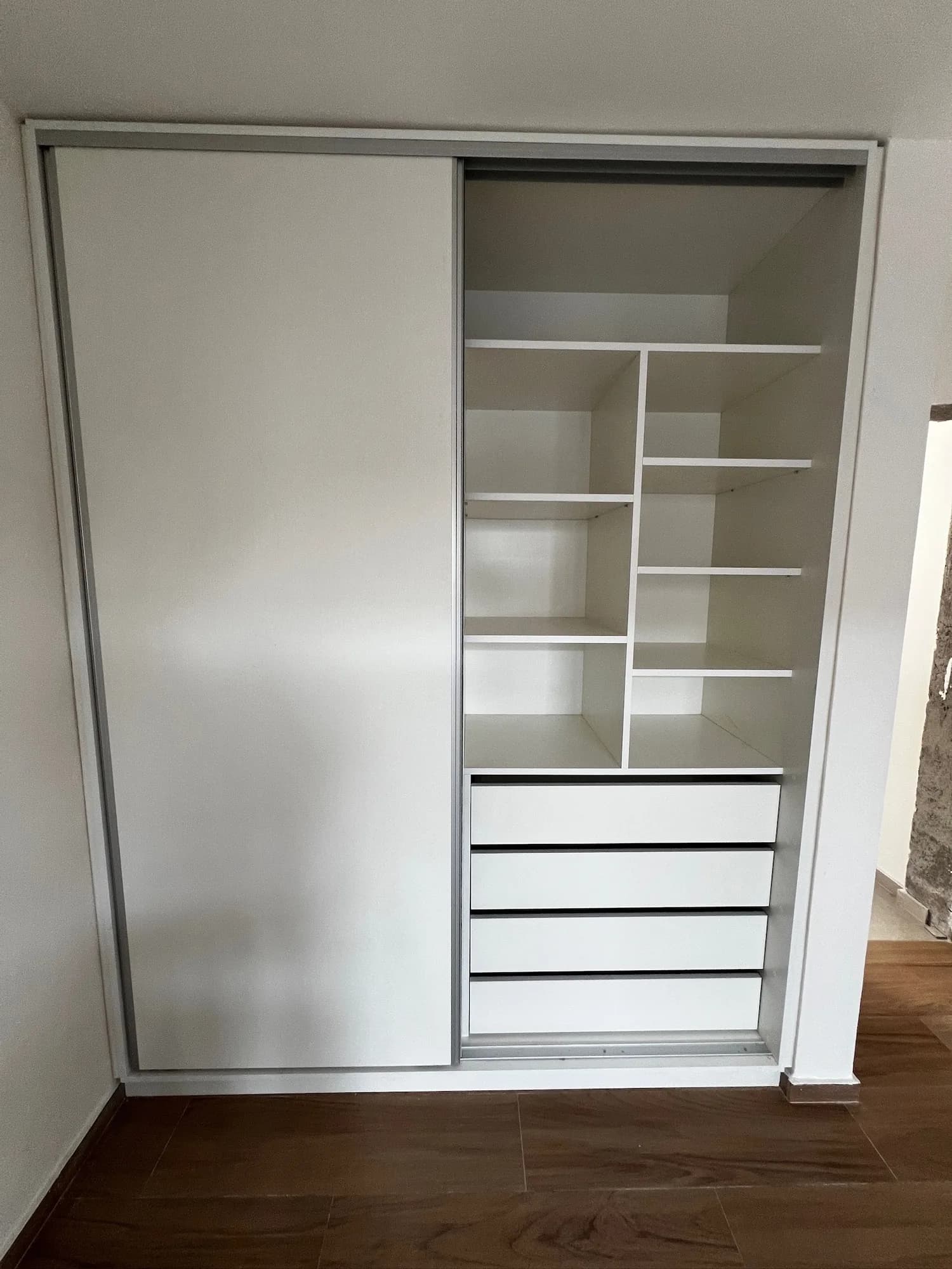 Placar empotrado blanco con una puerta corrediza y el interior abierto con estantes de distintas alturas y cuatro cajones; toma frontal