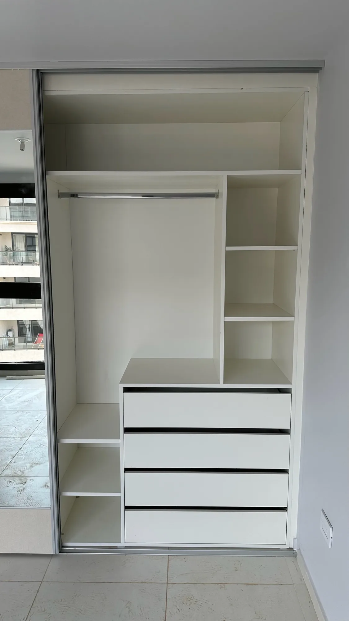 Interior de placard blanco con barral, estantes y cuatro cajones, junto a una puerta corrediza con espejo y perfilería de aluminio; toma frontal