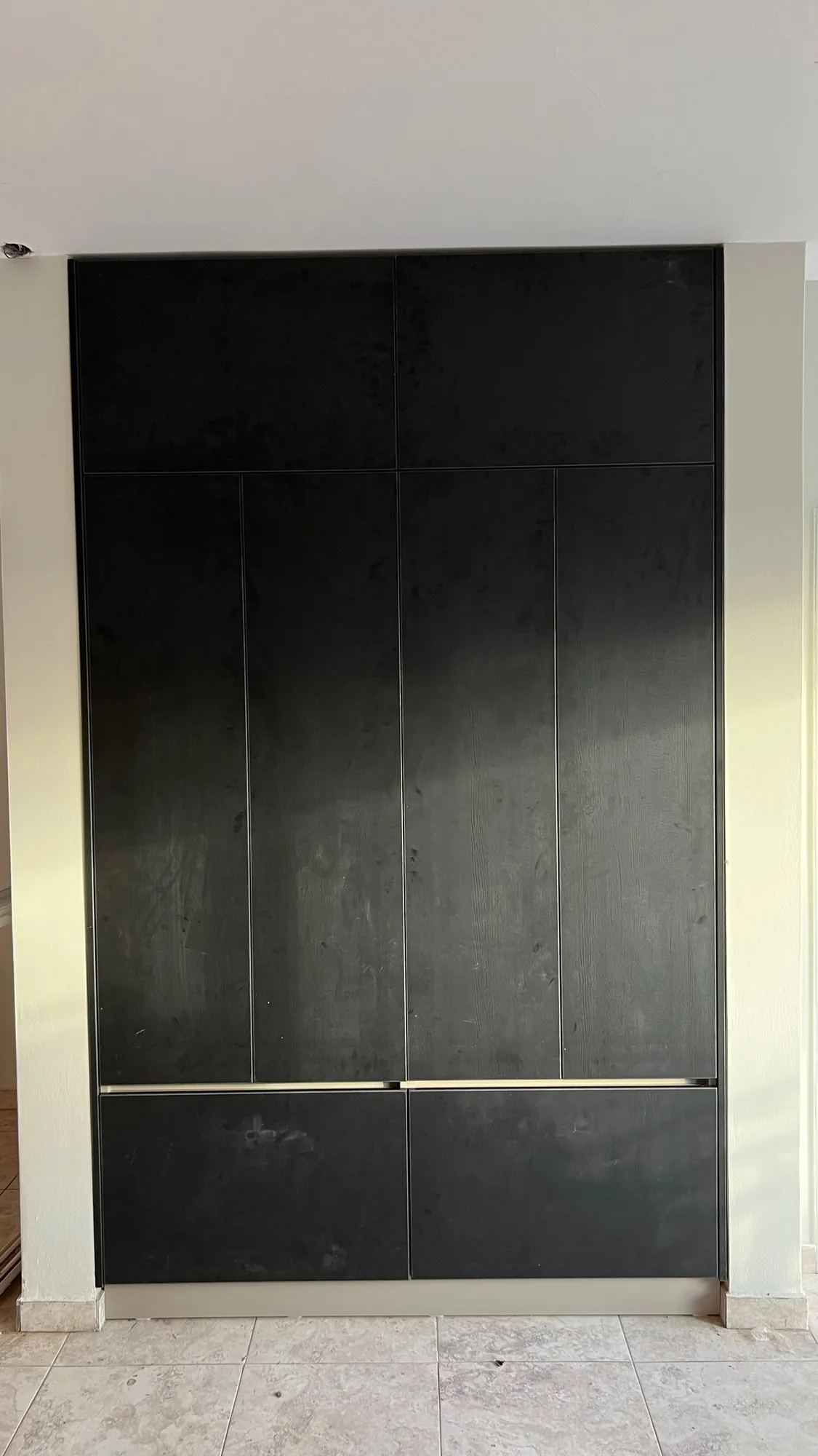 Mueble alto de piso a techo con puertas lisas negras sin tiradores y dos cajones inferiores con tirador de aluminio, empotrado entre paredes; toma frontal