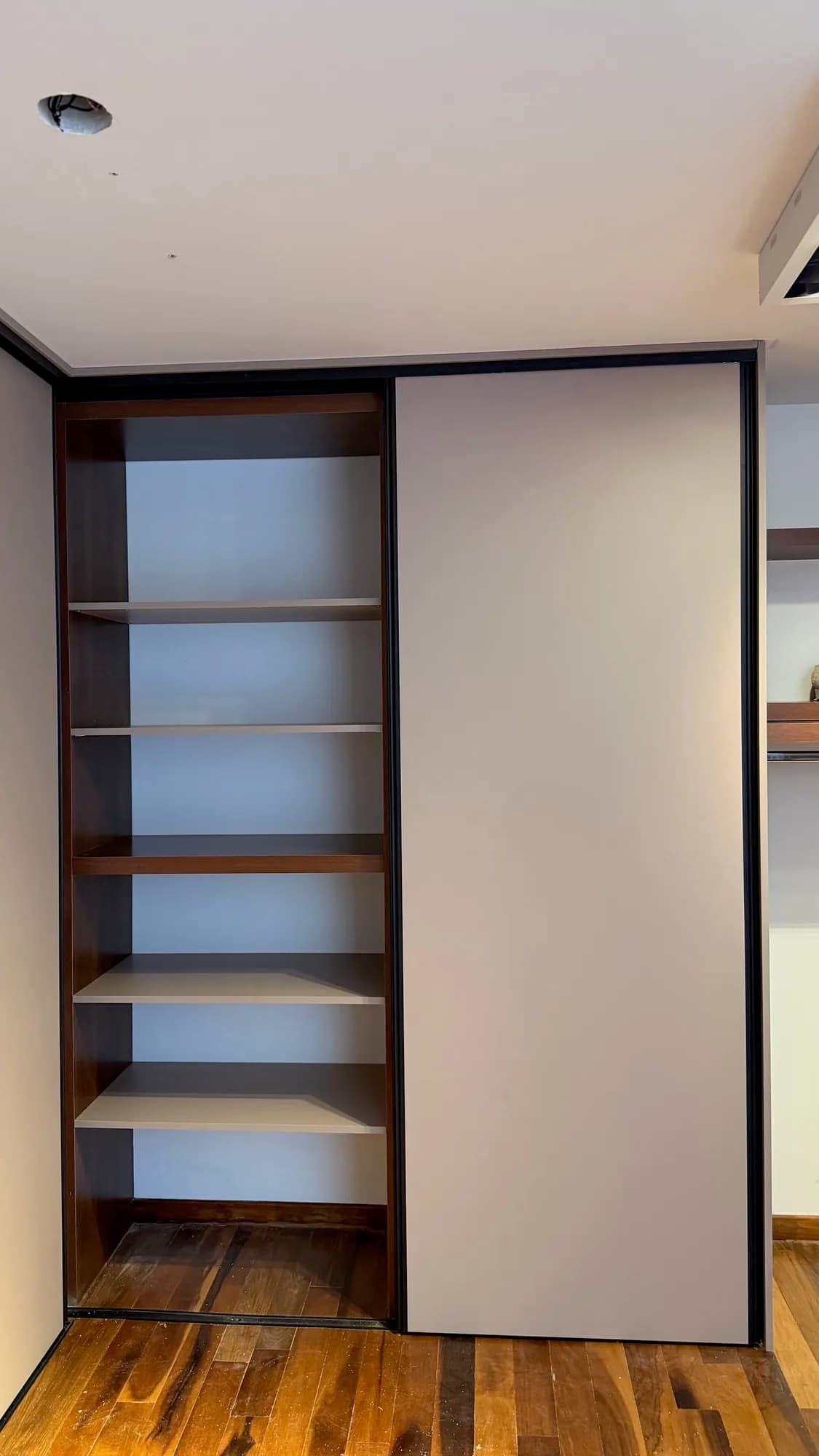 Placar con puerta corrediza beige y módulo abierto de estantes en nogal y beige, vacío; toma frontal sobre piso de madera