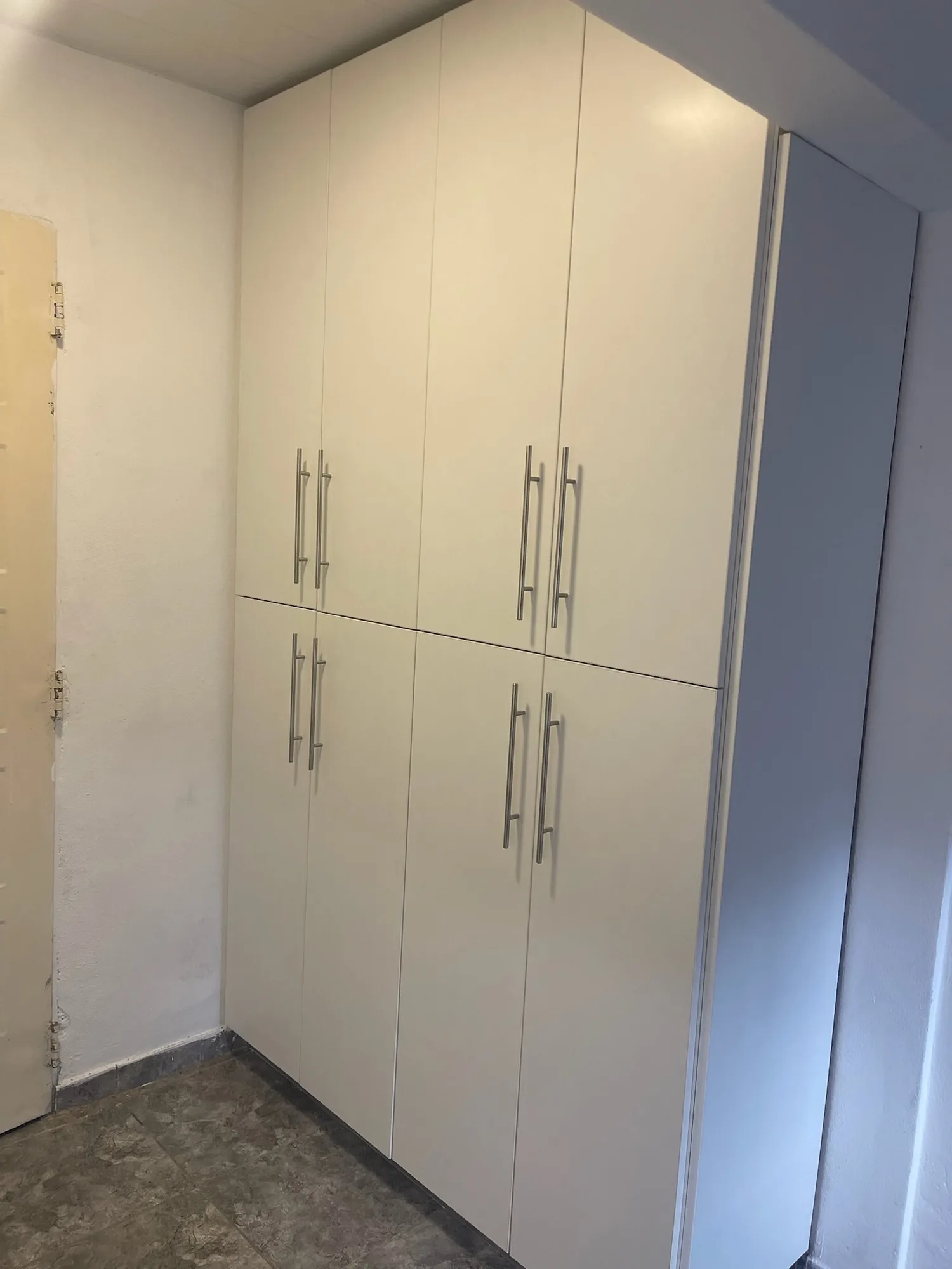 Mueble alto de ocho puertas en melamina blanca con tiradores de barra, instalado en una esquina junto a una puerta; toma en diagonal