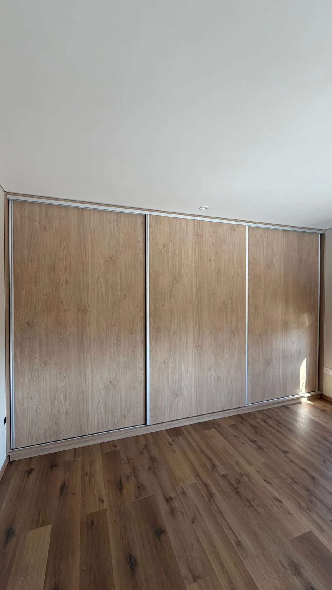 Placard empotrado de tres puertas corredizas en melamina símil roble con perfilería de aluminio, piso símil madera; toma frontal con puertas cerradas