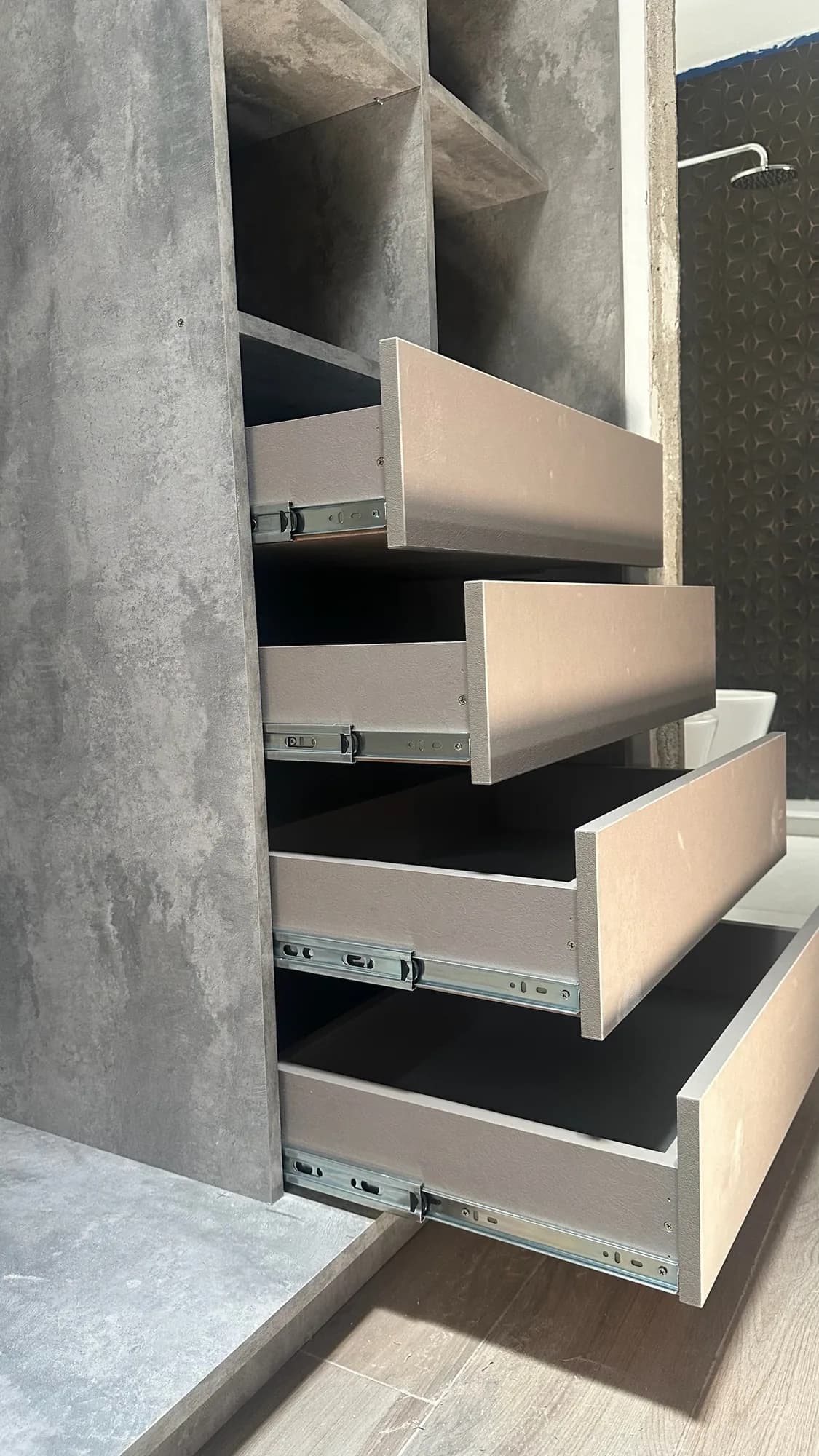 Detalle de cuatro cajones abiertos en melamina taupe con correderas metálicas telescópicas, dentro de un módulo símil hormigón; toma lateral en ángulo
