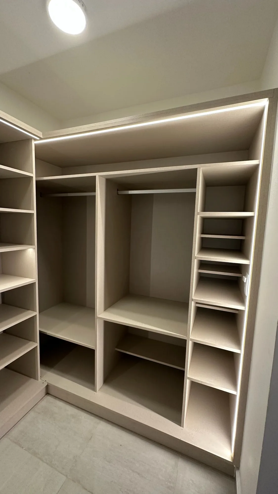 Vestidor abierto en melamina beige claro con dos tramos de colgado, estantes a la izquierda y columna de estantes inclinados a la derecha, con tira LED perimetral; toma frontal vertical