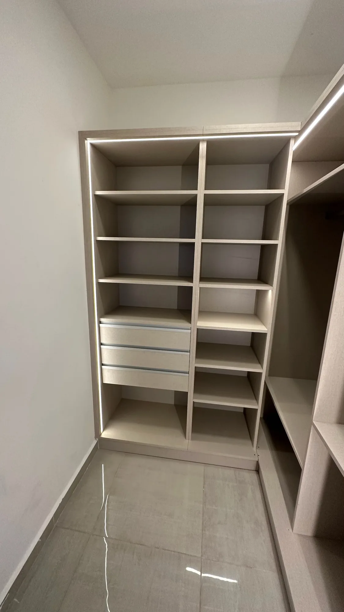 Módulo de vestidor en melamina beige claro con estantes, tres cajones con tirador de aluminio y tira LED en el borde superior e izquierdo; toma frontal vertical