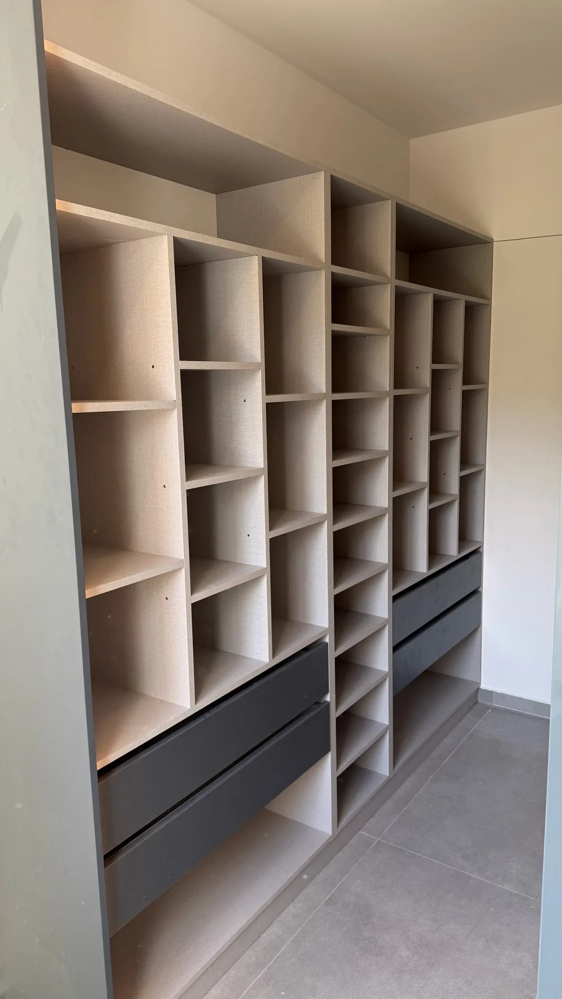 Vestidor con módulos de cubos y estantes de distinta altura en melamina gris beige con textura de tela y dos cajoneras con frente antracita, vistos en diagonal