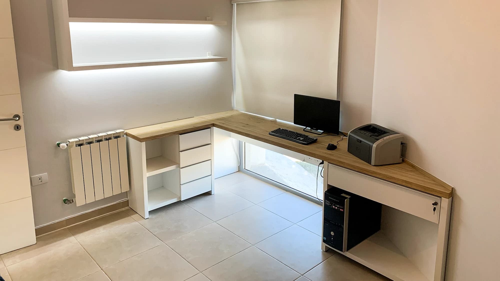 Escritorio en L con tapa de madera, cajonera blanca y estantes flotantes bajo la ventana