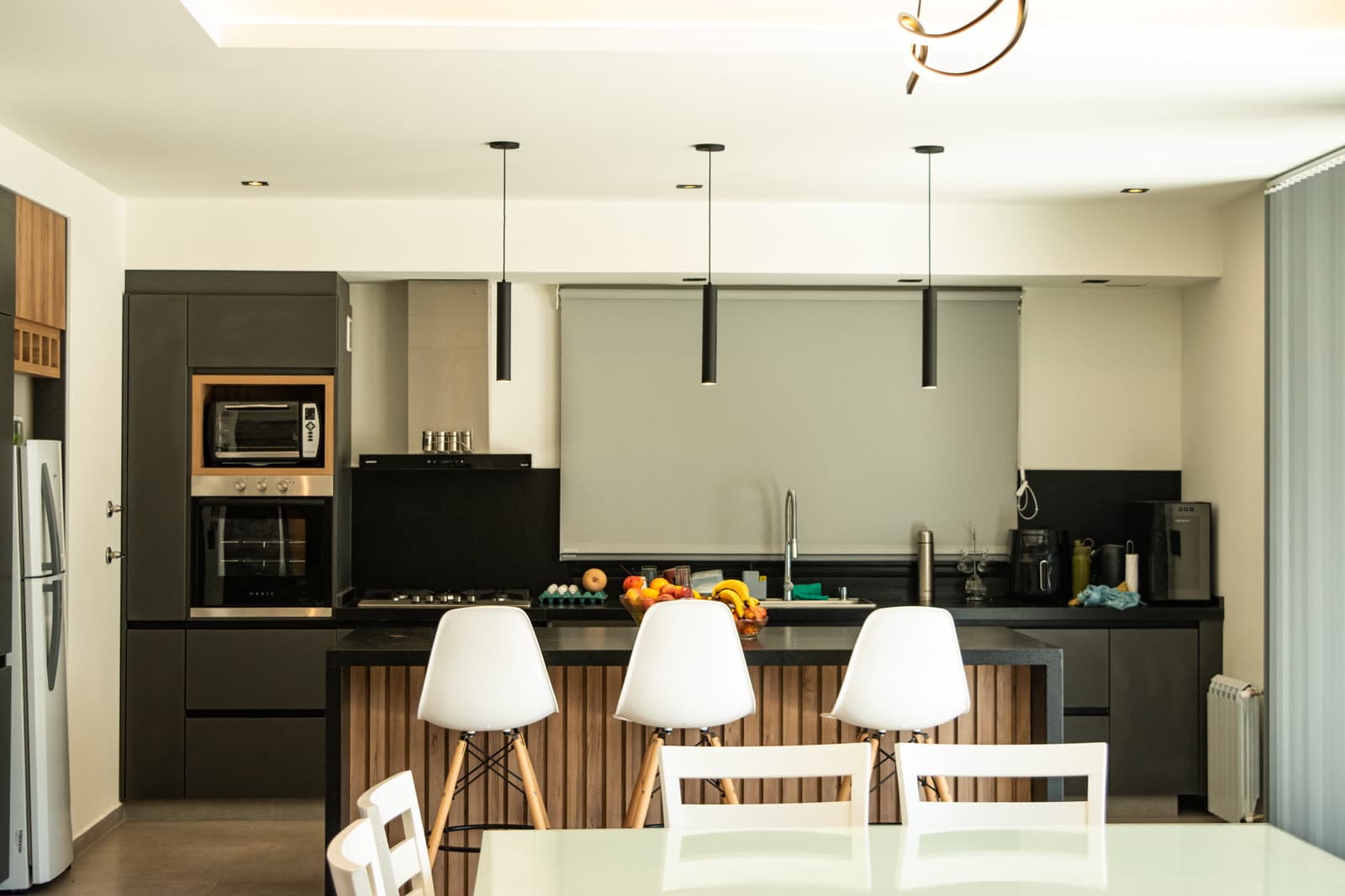 Cocina abierta con módulos altos grafito, bajo mesada de listones de madera y mesada negra