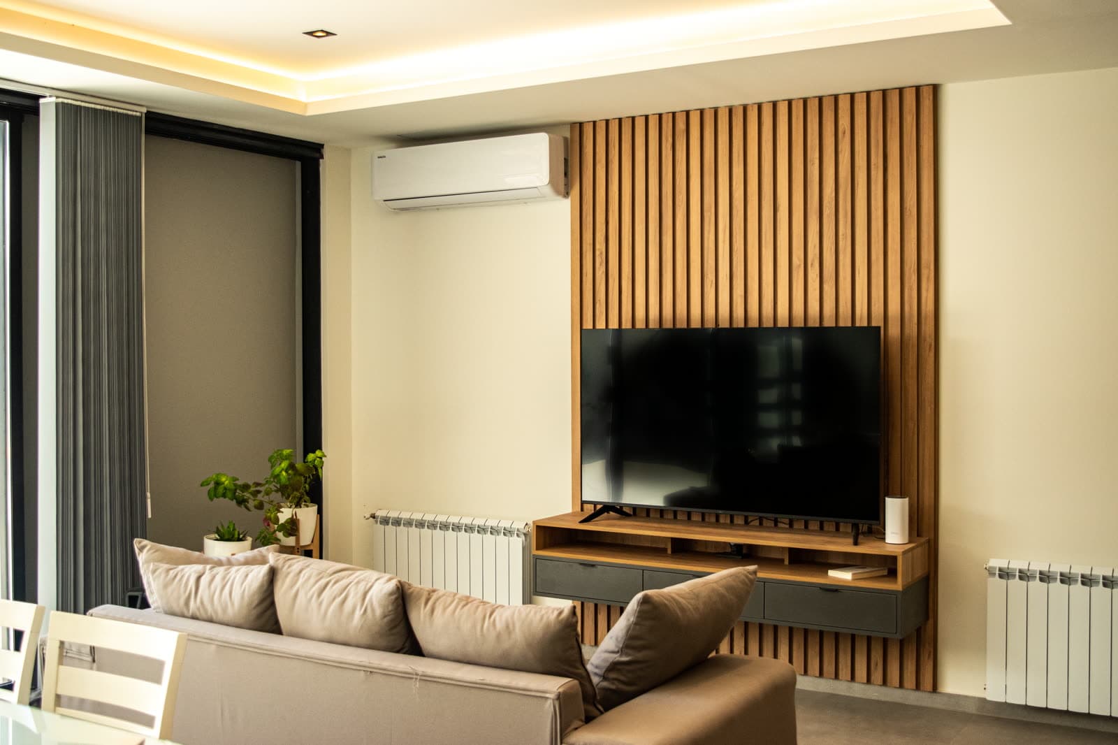 Panel de listones de madera con TV y mueble bajo flotante en un living luminoso